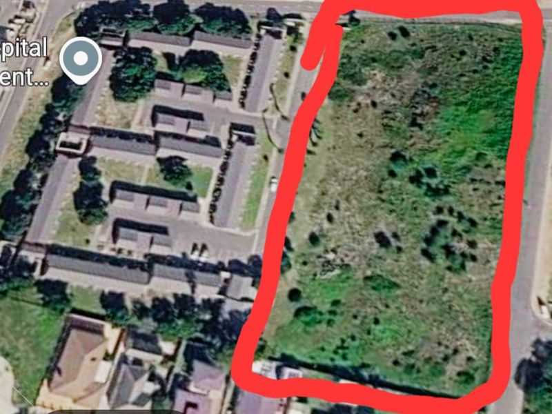An aerial view of a vacant residential plot of land, highlighted in red, situated in a developed neighborhood.