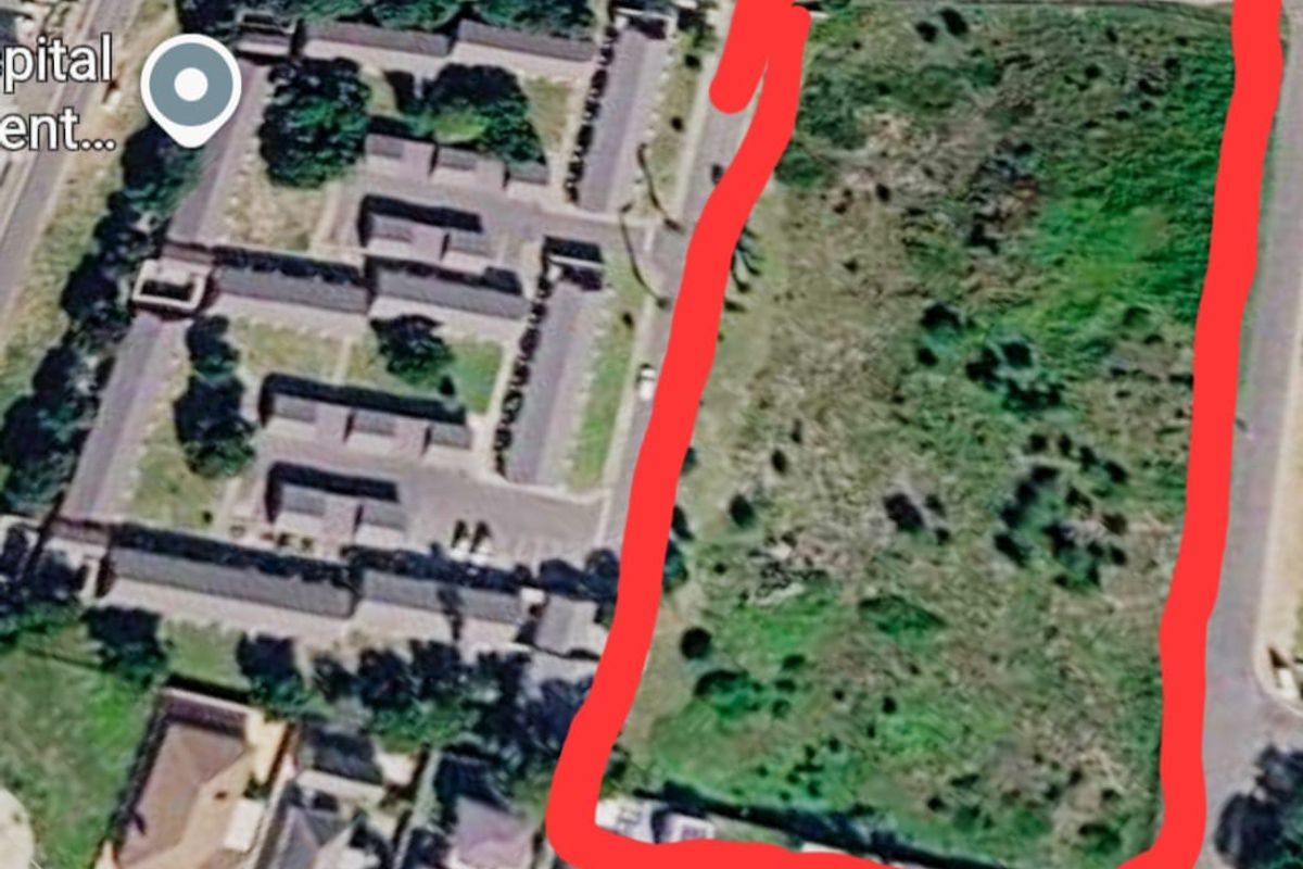 An aerial view of a vacant residential plot of land, highlighted in red, situated in a developed neighborhood.