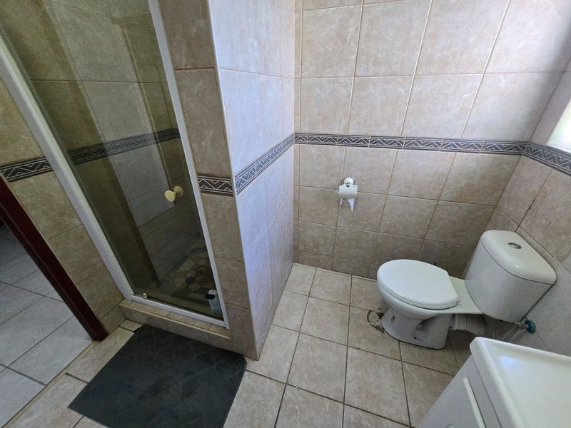 A functional bathroom featuring a glass shower enclosure, standard toilet, and neutral ceramic tiling with a decorative border.