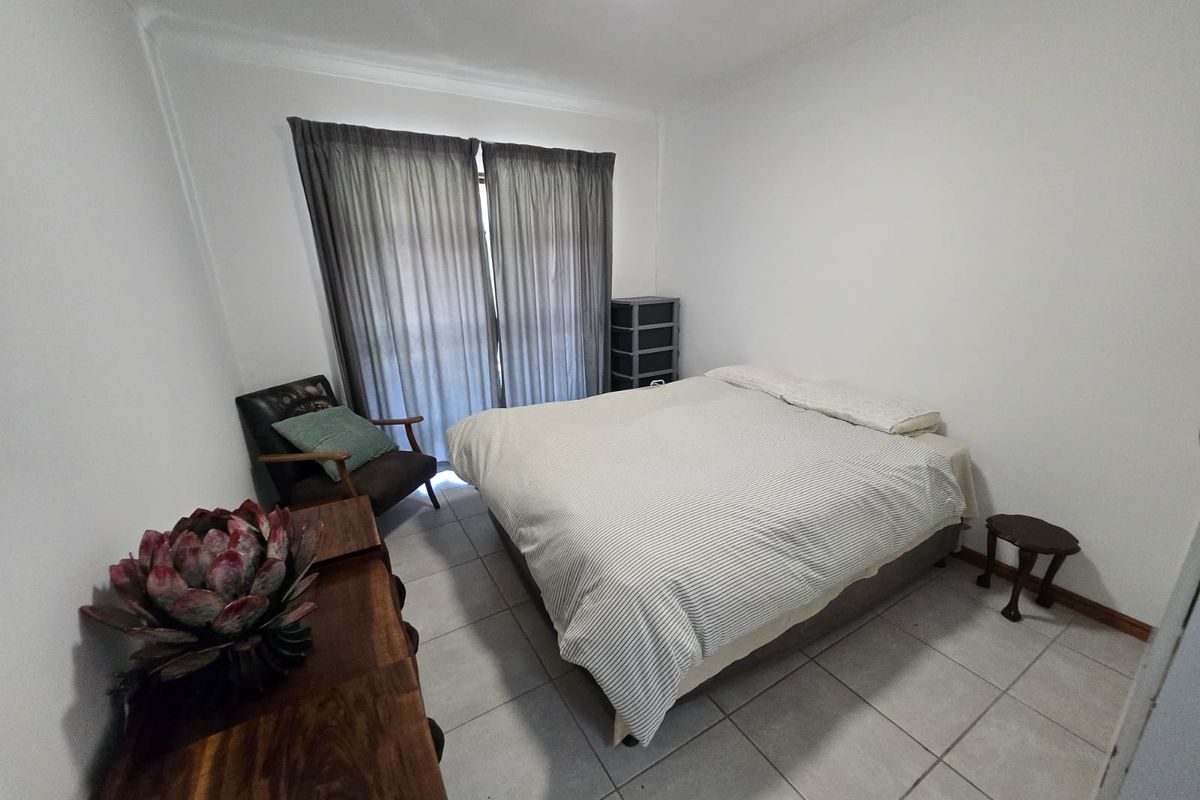 A functional bedroom featuring neutral tiled flooring, coved ceilings, and a sliding glass door providing access to the exterior.