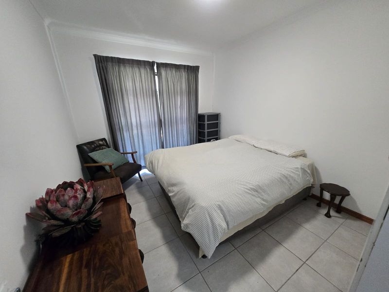 A functional bedroom featuring neutral tiled flooring, coved ceilings, and a sliding glass door providing access to the exterior.