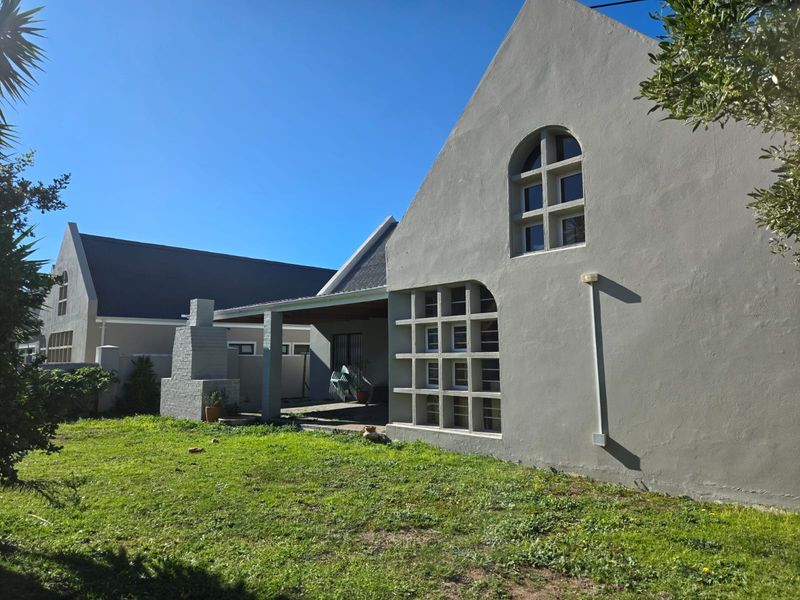 Rear view of the house featuring a covered patio, built-in braai, and unique architectural window detailing set against a spacious garden.