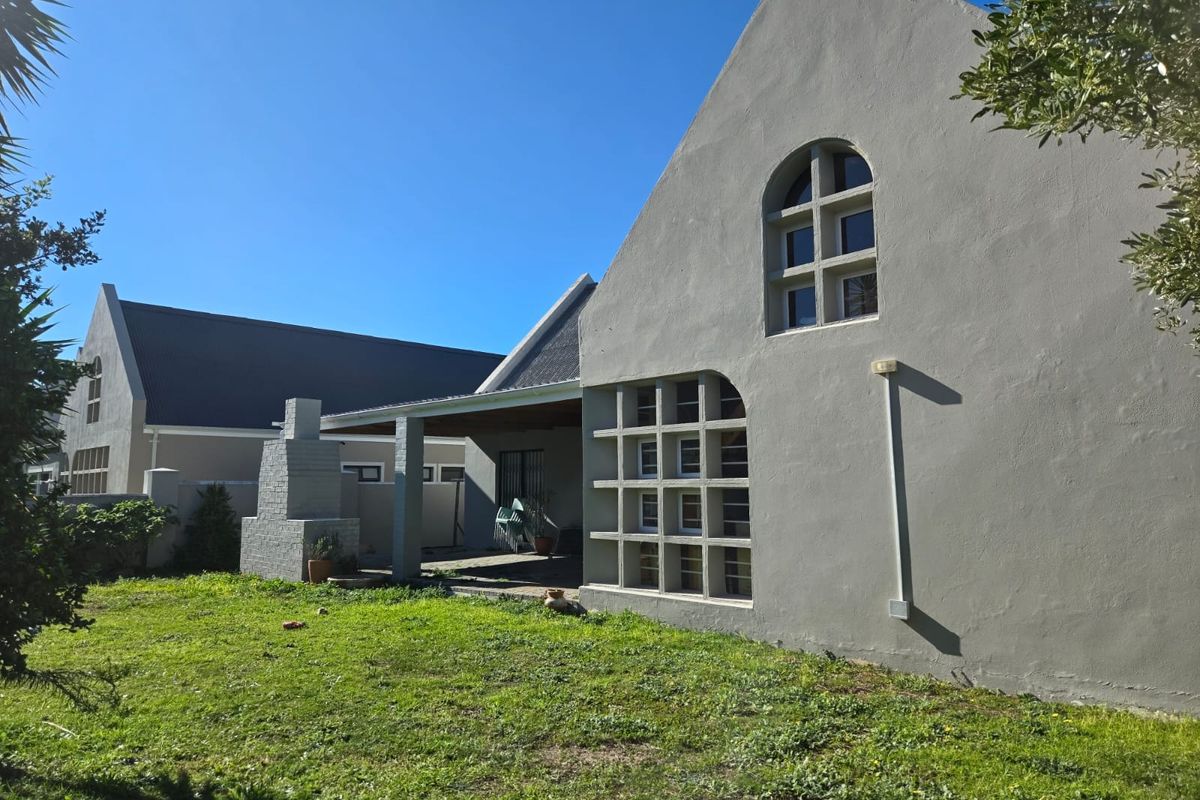 Rear view of the house featuring a covered patio, built-in braai, and unique architectural window detailing set against a spacious garden.