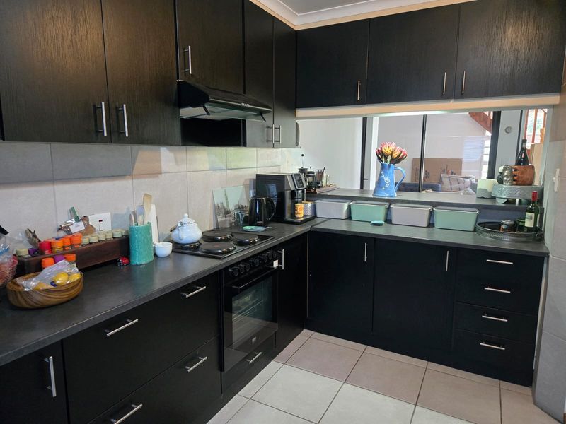 A functional kitchen featuring dark cabinetry, built-in oven and hob, extractor fan, and tiled flooring with a convenient serving hatch to the living area.