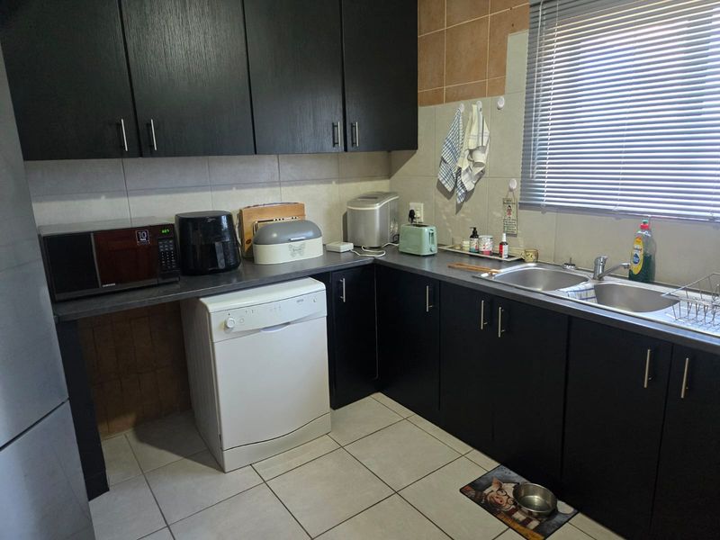 A functional kitchen featuring dark wood cabinetry, laminate countertops, a double stainless steel sink, and tiled finishes throughout.