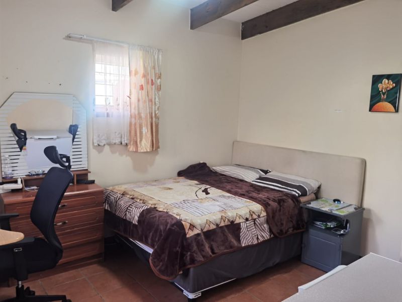 A bedroom featuring exposed timber ceiling beams and tiled flooring, offering a functional space with potential for cosmetic updates.