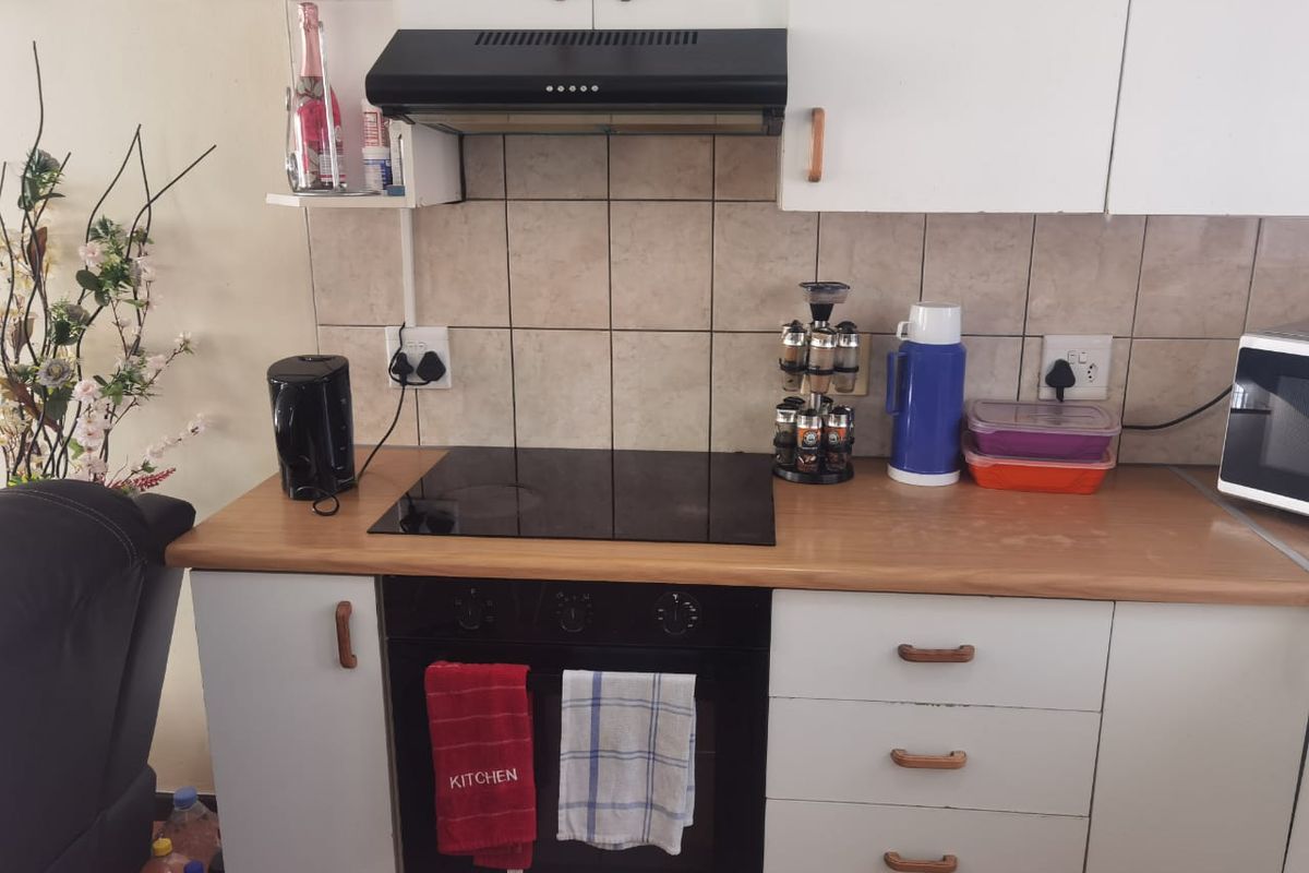 A functional kitchen area featuring a built-in oven, electric hob, extractor fan, tiled backsplash, and laminate countertops with ample storage cabinetry.