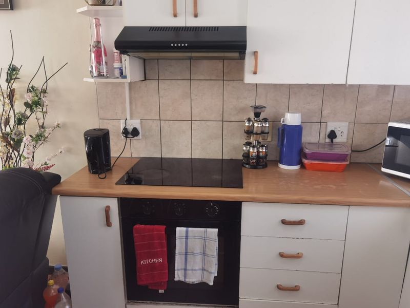 A functional kitchen area featuring a built-in oven, electric hob, extractor fan, tiled backsplash, and laminate countertops with ample storage cabinetry.