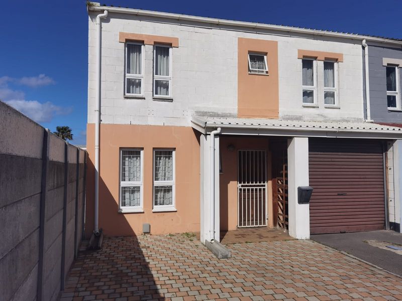 Front elevation of a two-story townhouse featuring a paved driveway, integrated garage with roller door, and secure gated entrance.