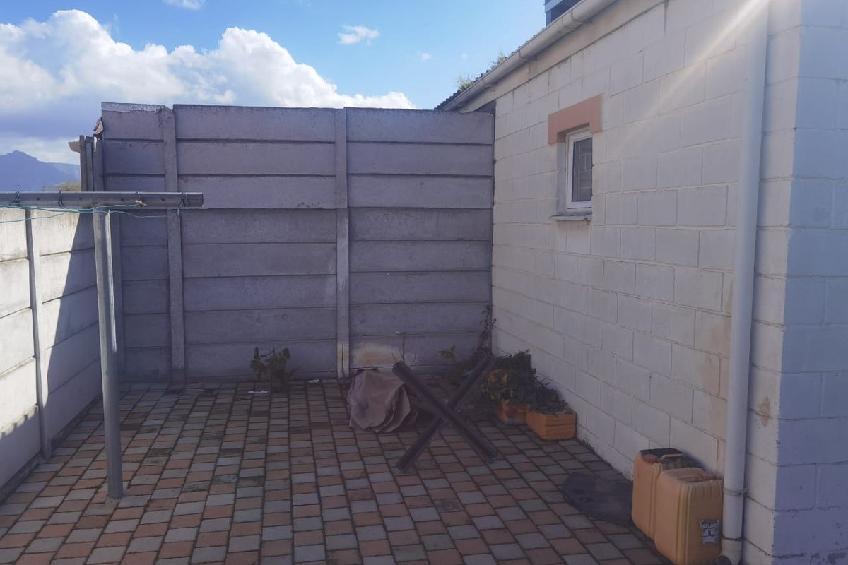 A paved rear courtyard area enclosed by precast concrete boundary walls, featuring a side exterior wall with a small window and drainage downpipe.