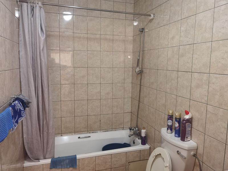 A functional bathroom featuring a bathtub with shower mixer, toilet, and full-height wall tiling.