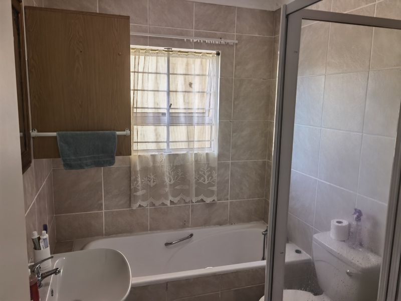 A functional bathroom featuring a bathtub, separate shower enclosure, toilet, and washbasin with neutral wall tiling.