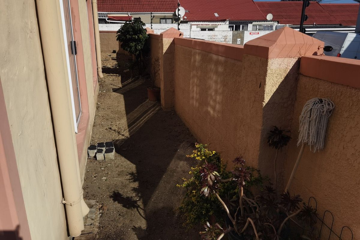 A narrow rear exterior side passage featuring a boundary wall and access to the apartment via a sliding door.