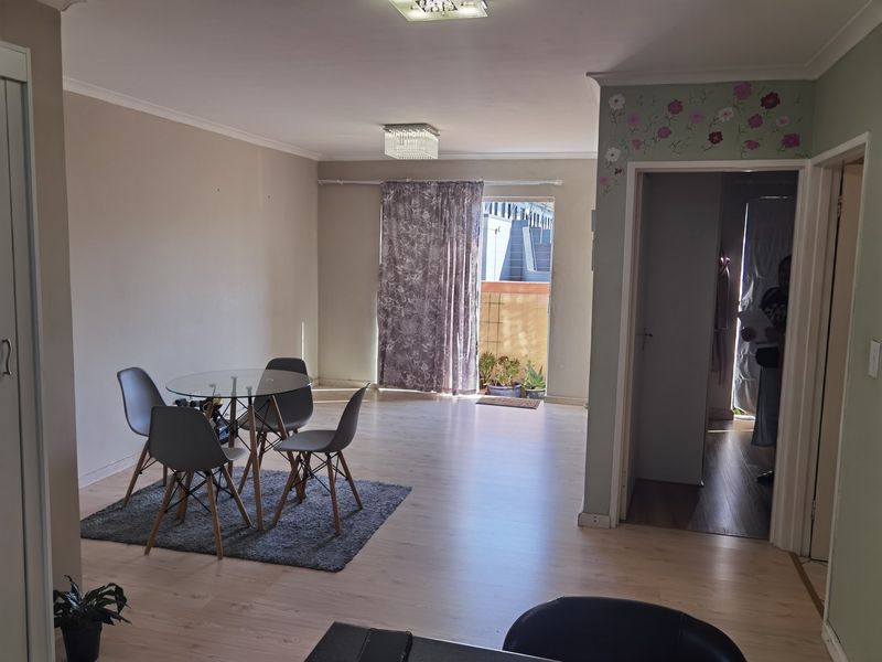 Open-plan living and dining area featuring light laminate flooring, neutral walls, and direct access to an outdoor balcony through a sliding door.