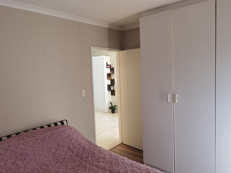 A bedroom featuring a built-in wardrobe and neutral wall finishes, with a view through the doorway into an adjacent room.