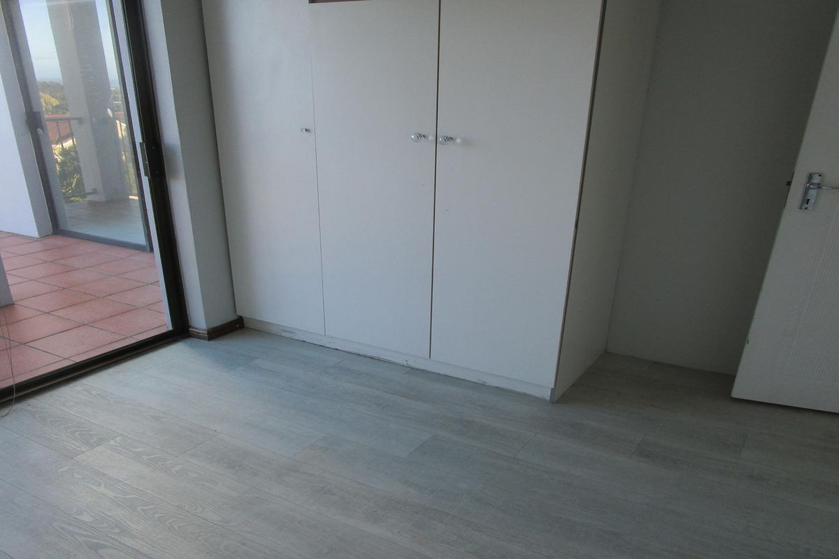 A bright, empty bedroom featuring light-toned laminate flooring, built-in cupboards, and a sliding glass door providing access to an outdoor patio area.