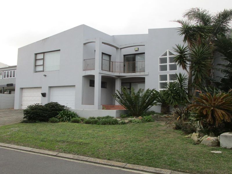 Front elevation of a multi-level residential property featuring a double garage, balcony, and established garden with paved driveway access.