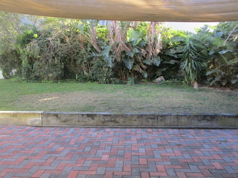 A paved patio area featuring a concrete retaining wall and a shade sail, overlooking a private garden space.
