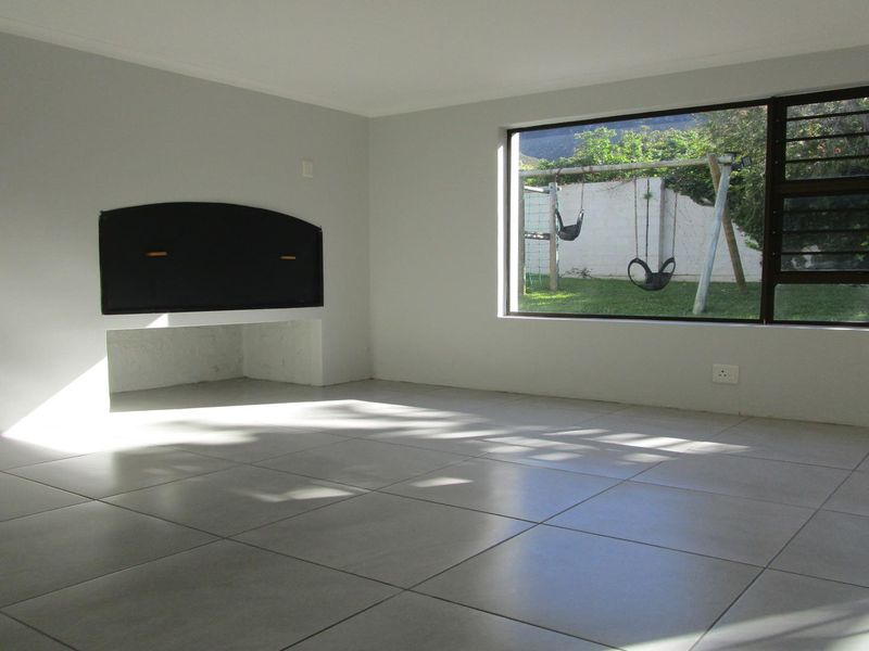A bright, empty living room featuring neutral tiled flooring, a built-in fireplace, and a large window overlooking the garden.