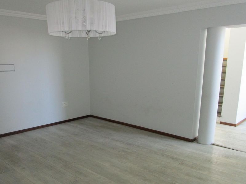 An empty living room featuring light-toned laminate flooring, crown molding, and a structural column leading to an adjacent space.
