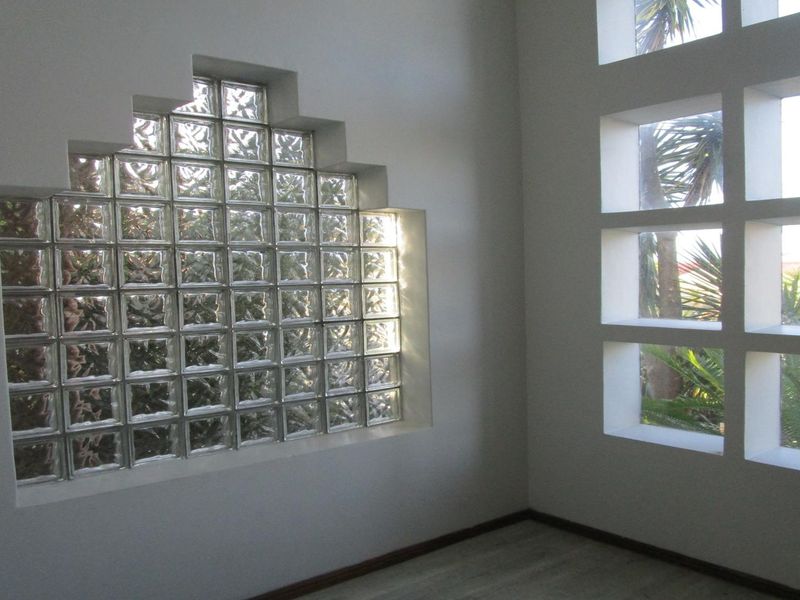 An empty living space featuring a unique stepped glass block window and a grid-pattern window, providing natural light and architectural interest.