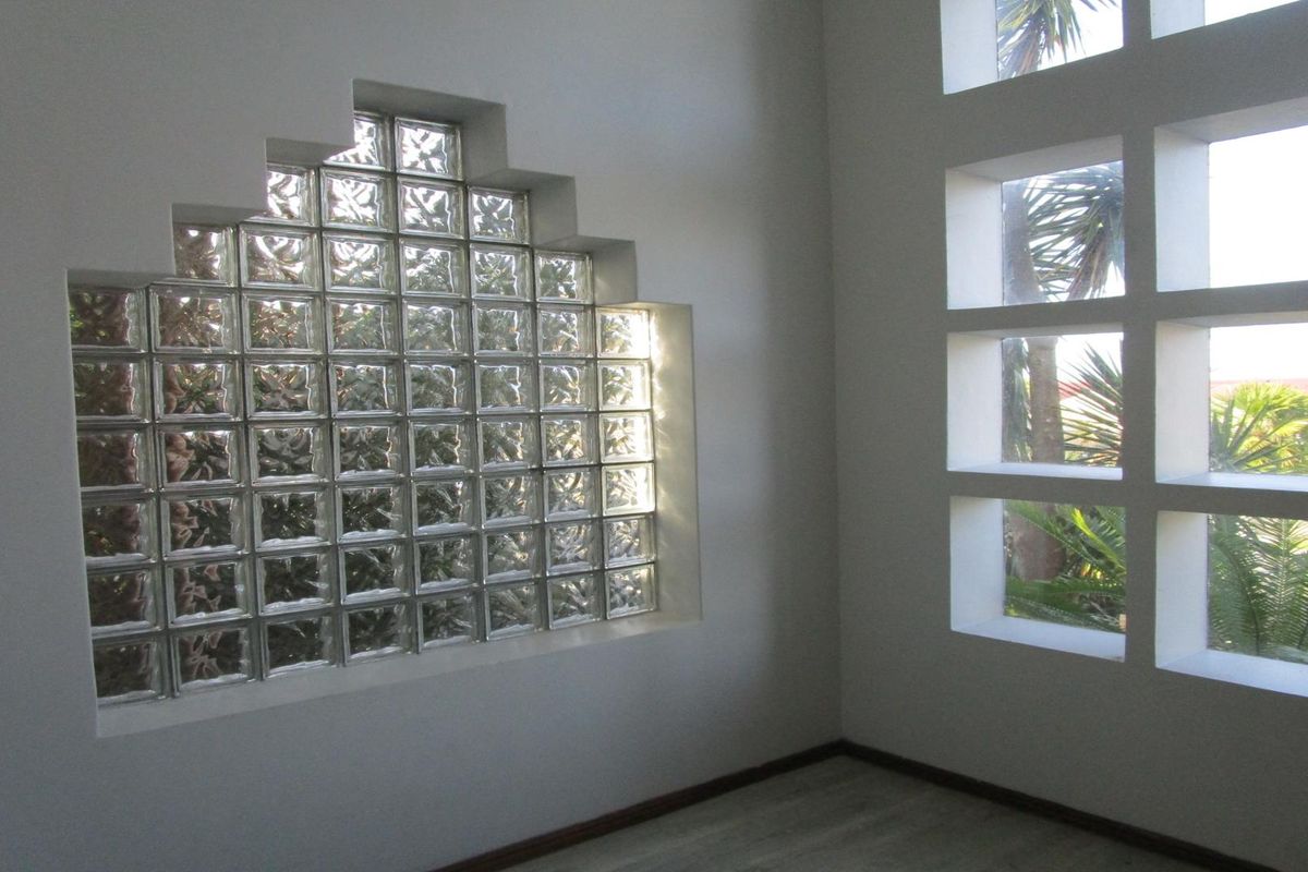 An empty living space featuring a unique stepped glass block window and a grid-pattern window, providing natural light and architectural interest.
