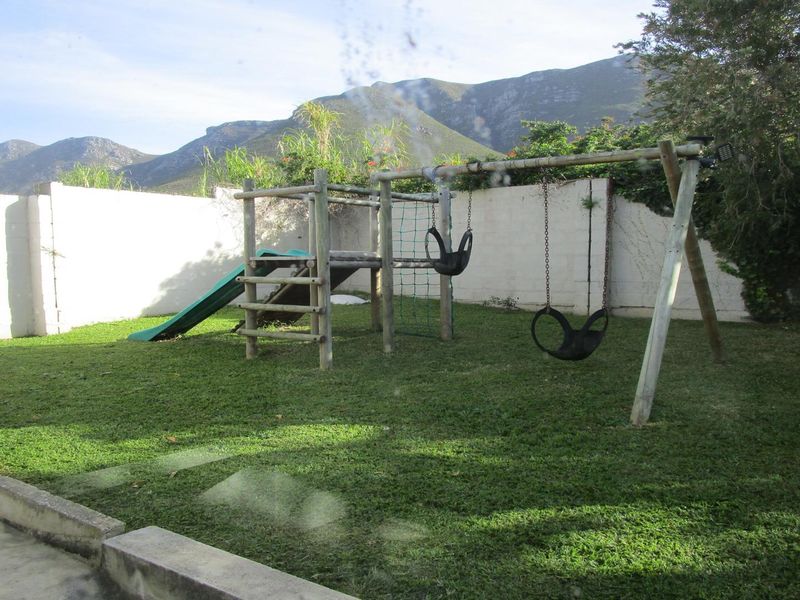 A private rear garden featuring a lawn area, perimeter boundary walls, and mountain views, captured through a window with some surface smudges.