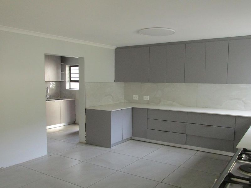 Modern kitchen featuring sleek grey cabinetry, stone countertops, a gas hob, and an adjoining scullery area with matching finishes.