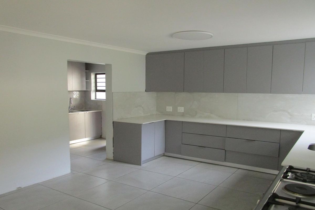 Modern kitchen featuring sleek grey cabinetry, stone countertops, a gas hob, and an adjoining scullery area with matching finishes.