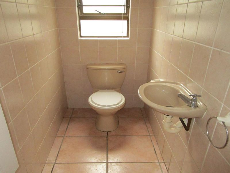 A compact, dated bathroom featuring neutral ceramic wall and floor tiles, a wall-mounted basin, and a standard toilet.