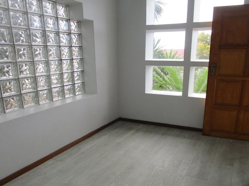 An empty entrance area featuring a distinctive glass block wall, grid-style window, and light-toned laminate flooring.