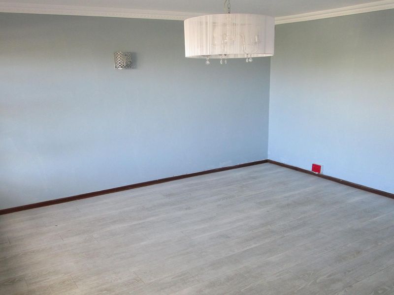 A bright, empty living room featuring light-toned laminate flooring, coving, and modern lighting fixtures, providing a clean and neutral canvas for interior design.