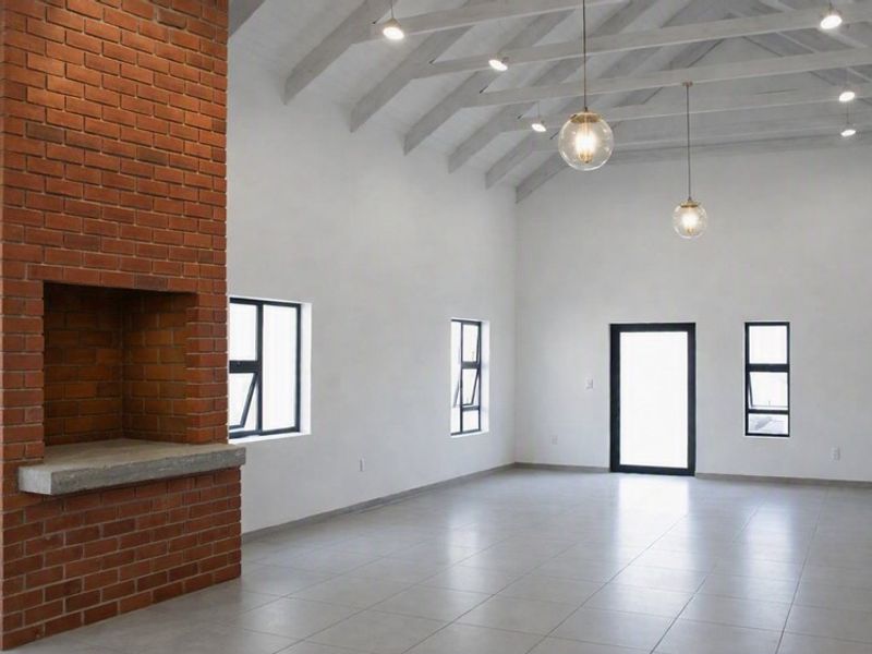 Spacious living area featuring a striking exposed brick fireplace, vaulted ceilings with exposed beams, tiled floors, and modern lighting fixtures.