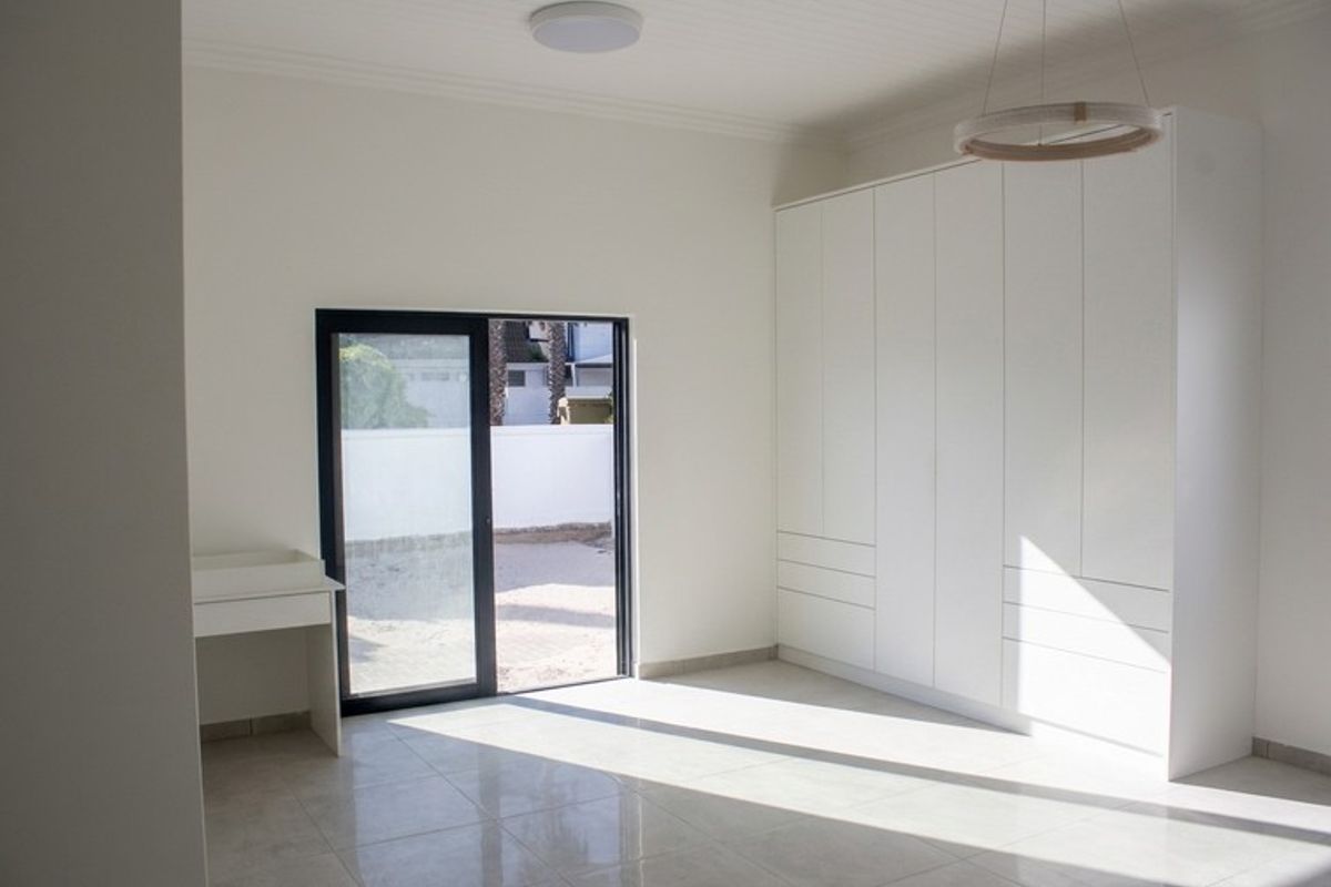 A bright, modern bedroom featuring neutral tiled floors, extensive built-in cabinetry, and a sliding glass door providing direct access to the outdoor area.