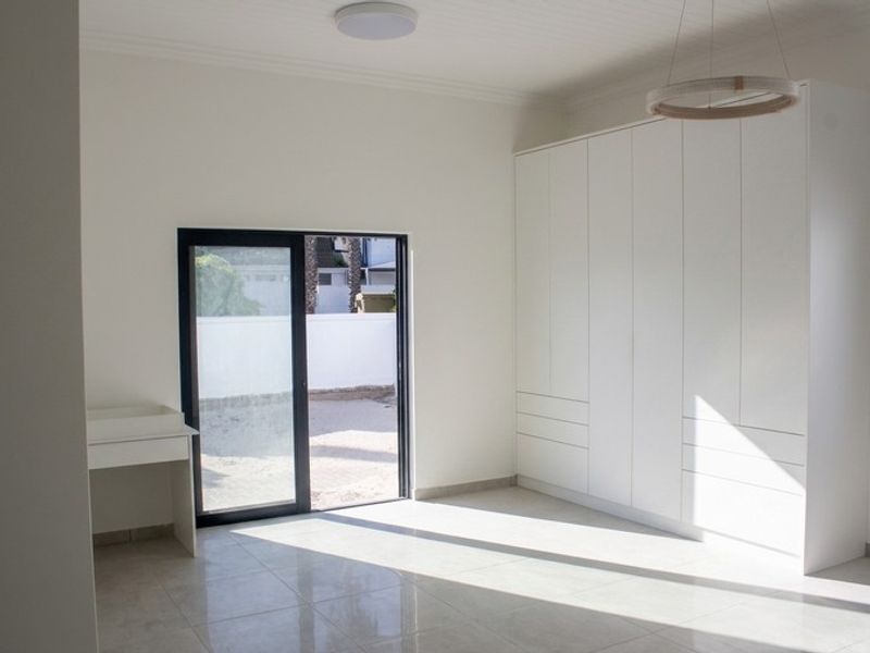 A bright, modern bedroom featuring neutral tiled floors, extensive built-in cabinetry, and a sliding glass door providing direct access to the outdoor area.