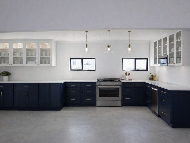 A modern, well-appointed kitchen featuring navy blue base cabinetry, white quartz countertops, stainless steel appliances, and elegant glass-front upper cabinets.
