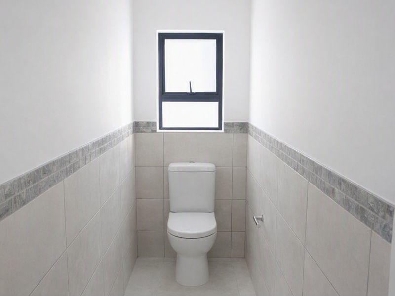 A clean and modern guest toilet featuring neutral wall and floor tiles with a decorative border and a window for natural light.