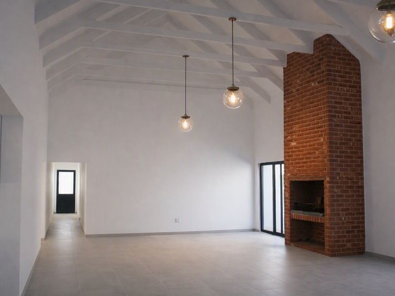 Spacious living area featuring high vaulted ceilings with exposed rafters, a prominent brick fireplace, and modern tiled flooring.