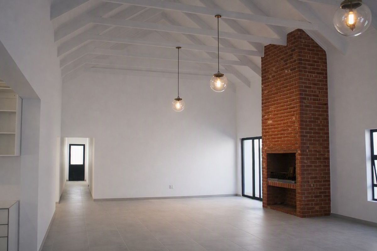 Spacious living area featuring high vaulted ceilings with exposed rafters, a prominent brick fireplace, and modern tiled flooring.