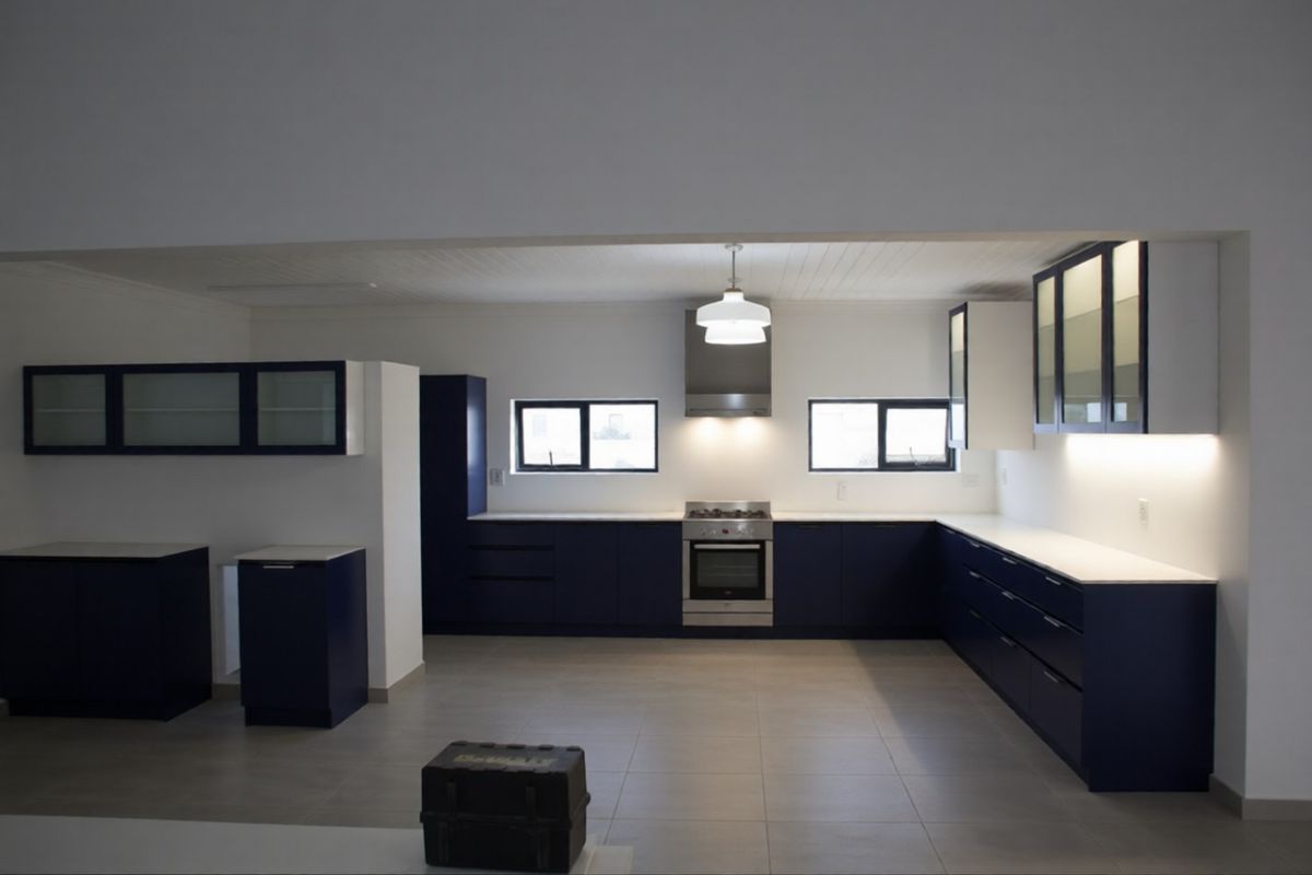 Modern, spacious kitchen featuring dark blue cabinetry, stone countertops, integrated stainless steel appliances, and ample under-cabinet lighting.