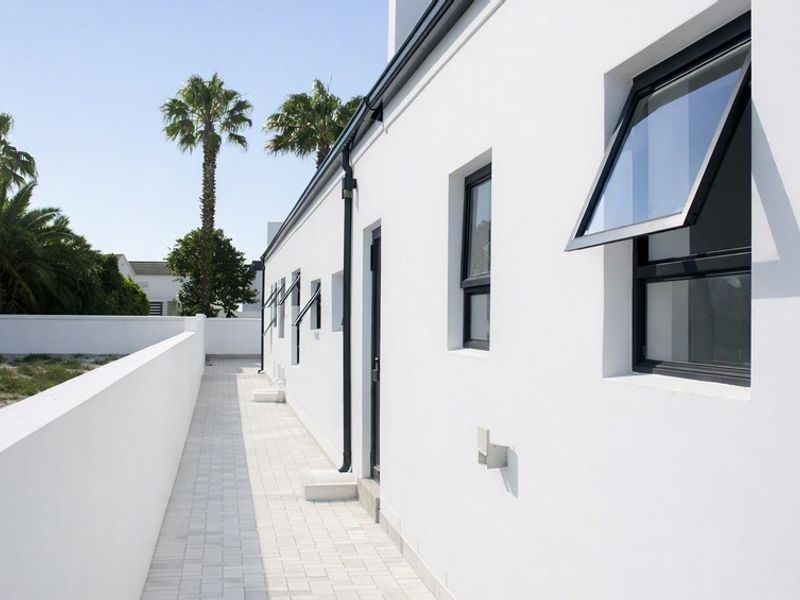 A clean, modern exterior rear walkway featuring white rendered walls, dark-framed casement windows, and paved flooring along the side of the property.