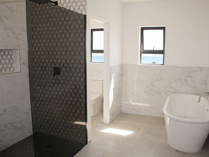 Modern bathroom featuring a freestanding bathtub, walk-in shower with decorative tiling, and a separate toilet area with ocean views.
