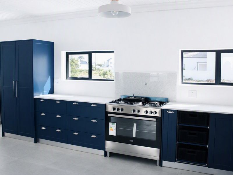 Modern kitchen featuring navy blue cabinetry, stone countertops, and a stainless steel gas stove with oven.