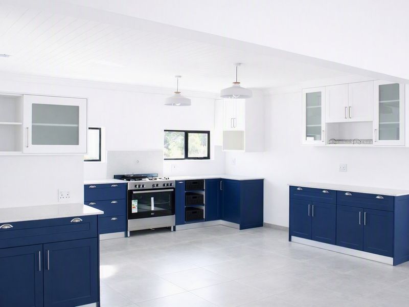 A modern, spacious kitchen featuring navy blue cabinetry, white stone countertops, a gas stove, and clean tiled flooring in a bright, open-plan layout.