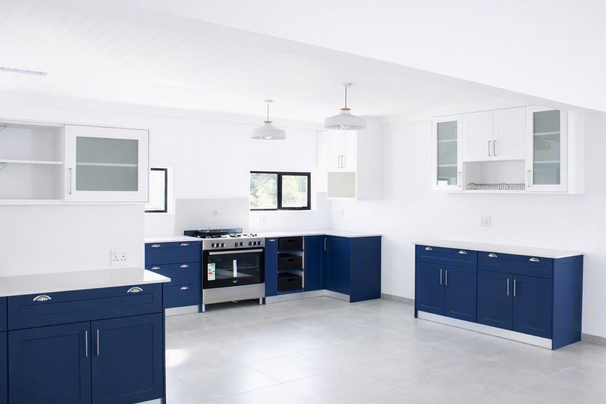 A modern, spacious kitchen featuring navy blue cabinetry, white stone countertops, a gas stove, and clean tiled flooring in a bright, open-plan layout.