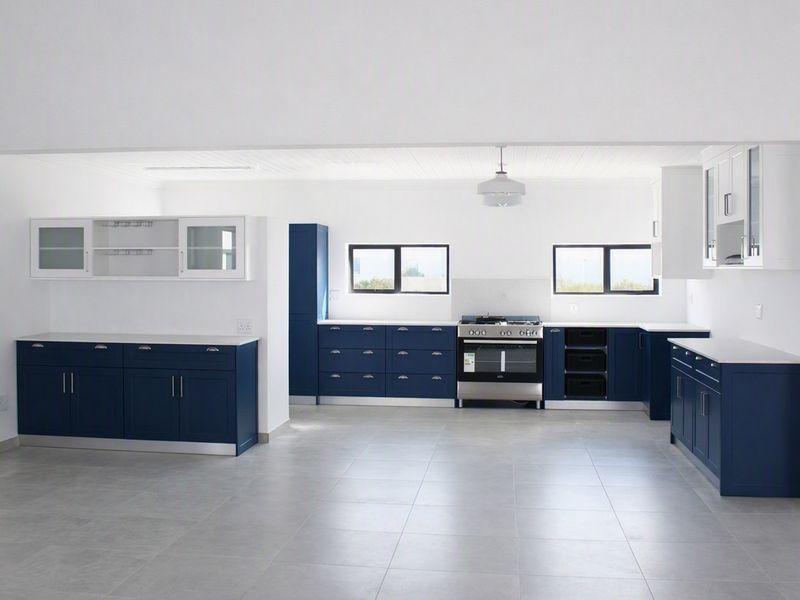 A spacious, modern kitchen featuring navy blue cabinetry, white countertops, tiled flooring, and a built-in gas stove with oven.