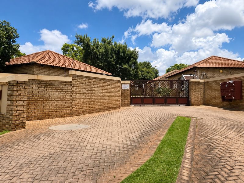 Front entrance view of the townhouse complex featuring a secure gated access point, brick boundary walls, and a paved driveway.