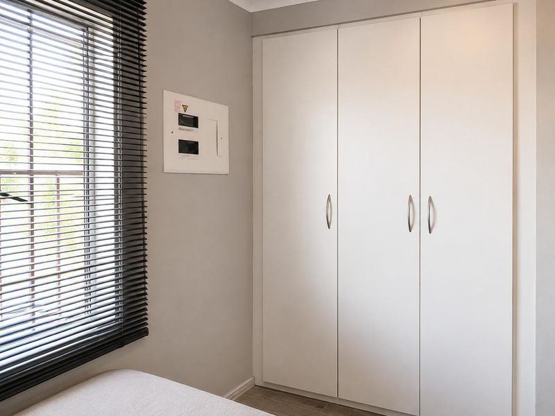 A clean, neutral bedroom featuring a built-in wardrobe, electrical distribution board, and venetian blinds, offering a functional and well-maintained space.