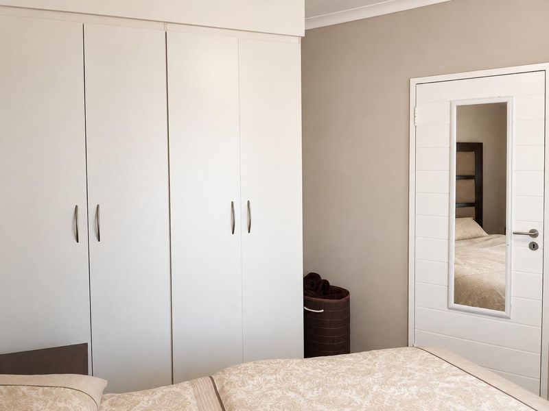 A well-maintained bedroom featuring floor-to-ceiling built-in cupboards and a modern internal door with an integrated full-length mirror.