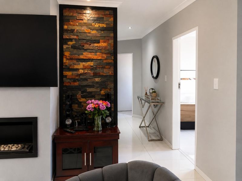A modern living room featuring a striking stone accent wall, built-in fireplace, and polished tile flooring, leading into a bright hallway.
